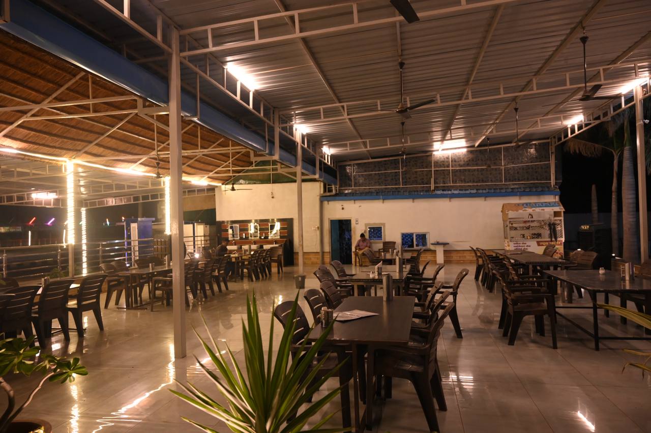 Covered open-sided dining area with tables under warm evening lighting.