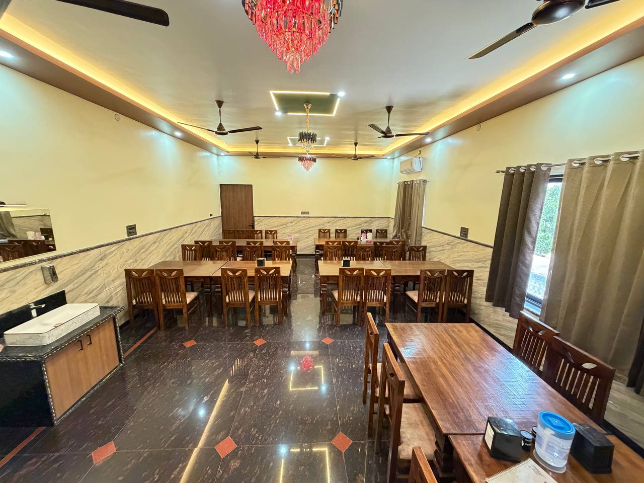 Indoor dining room with wooden tables, chairs and warm ceiling lighting.