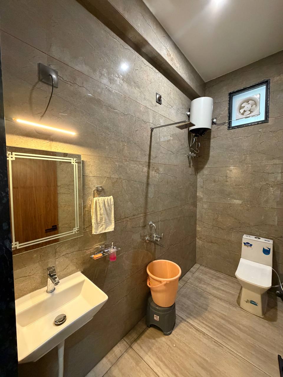 Tiled bathroom with basin, overhead shower, water heater and toilet.